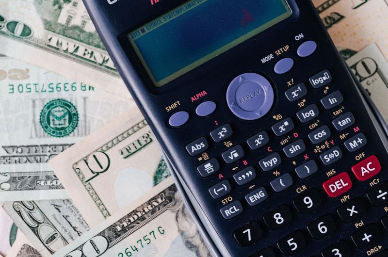 A calculator placed over a stack of currency, representing the budgeting process for advertising campaigns
