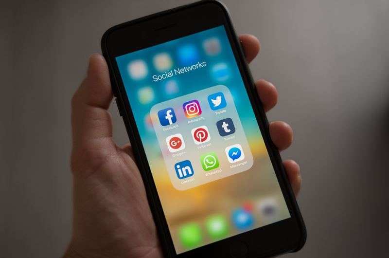 A person holding a phone showing social network apps, the platforms at the center of social media marketing