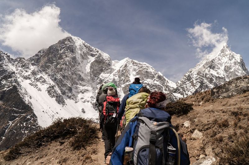 Hikers trekking on a sunny trail with snow-capped mountains behind, the adventure experiences travel SEO promotes
