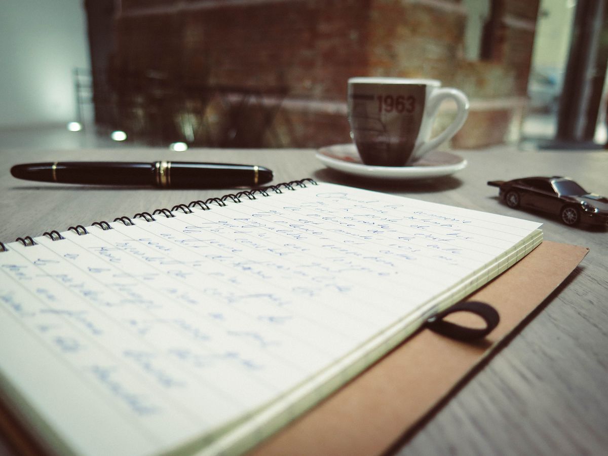 A writing desk with a notebook, pen and coffee, set up for planning content