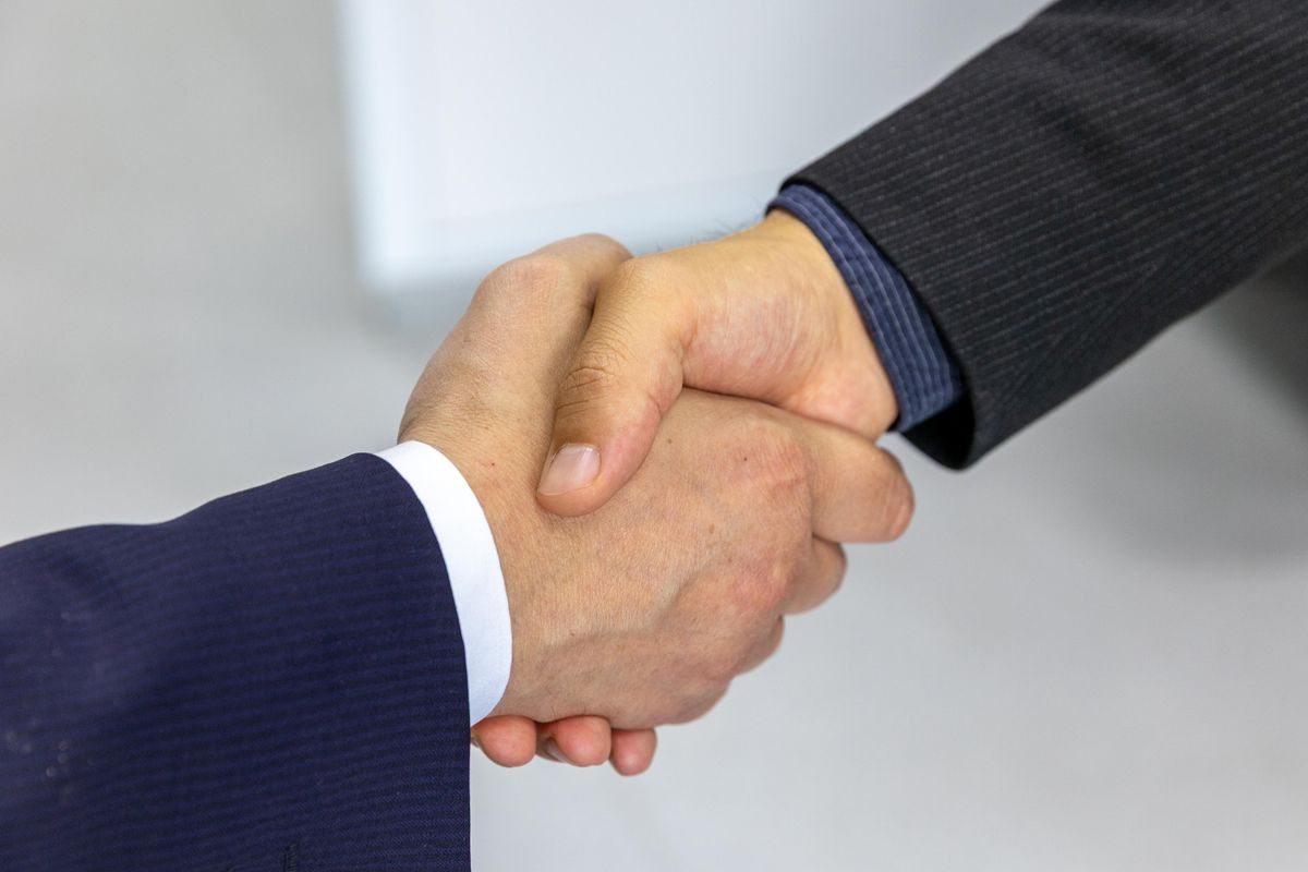 Two people shaking hands over a desk, sealing a working agreement