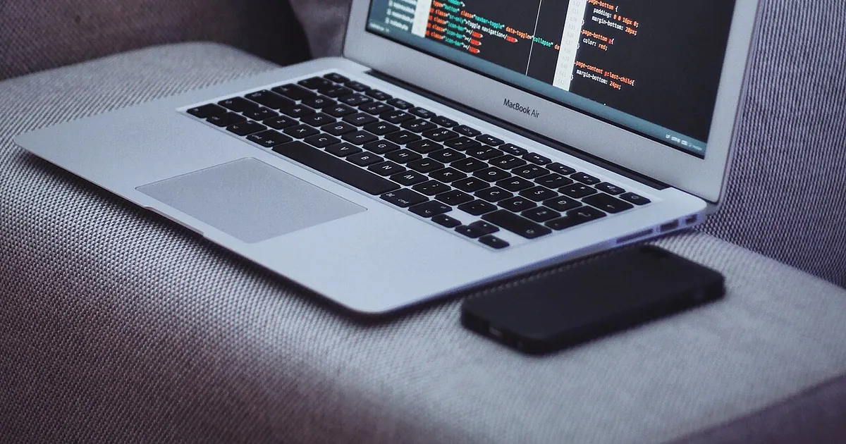 A laptop on a sofa displays a code editor