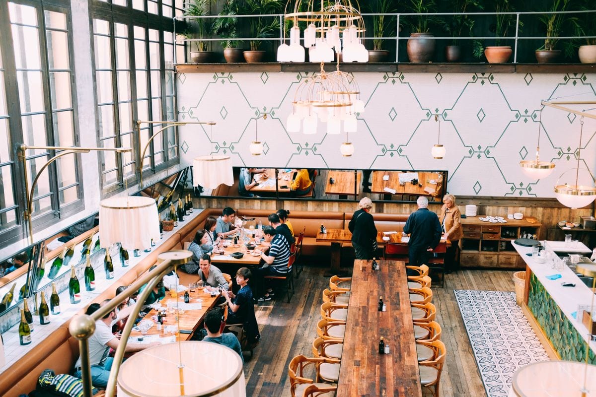 A busy restaurant dining room full of diners at warmly lit wooden tables