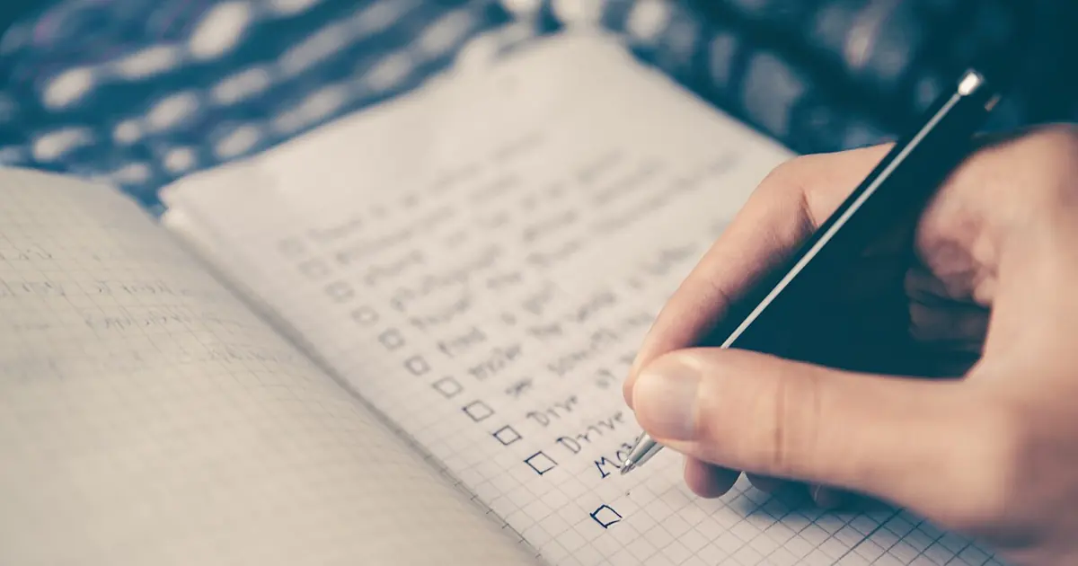 Person writing a checklist in a notebook, illustrating an SEO audit report