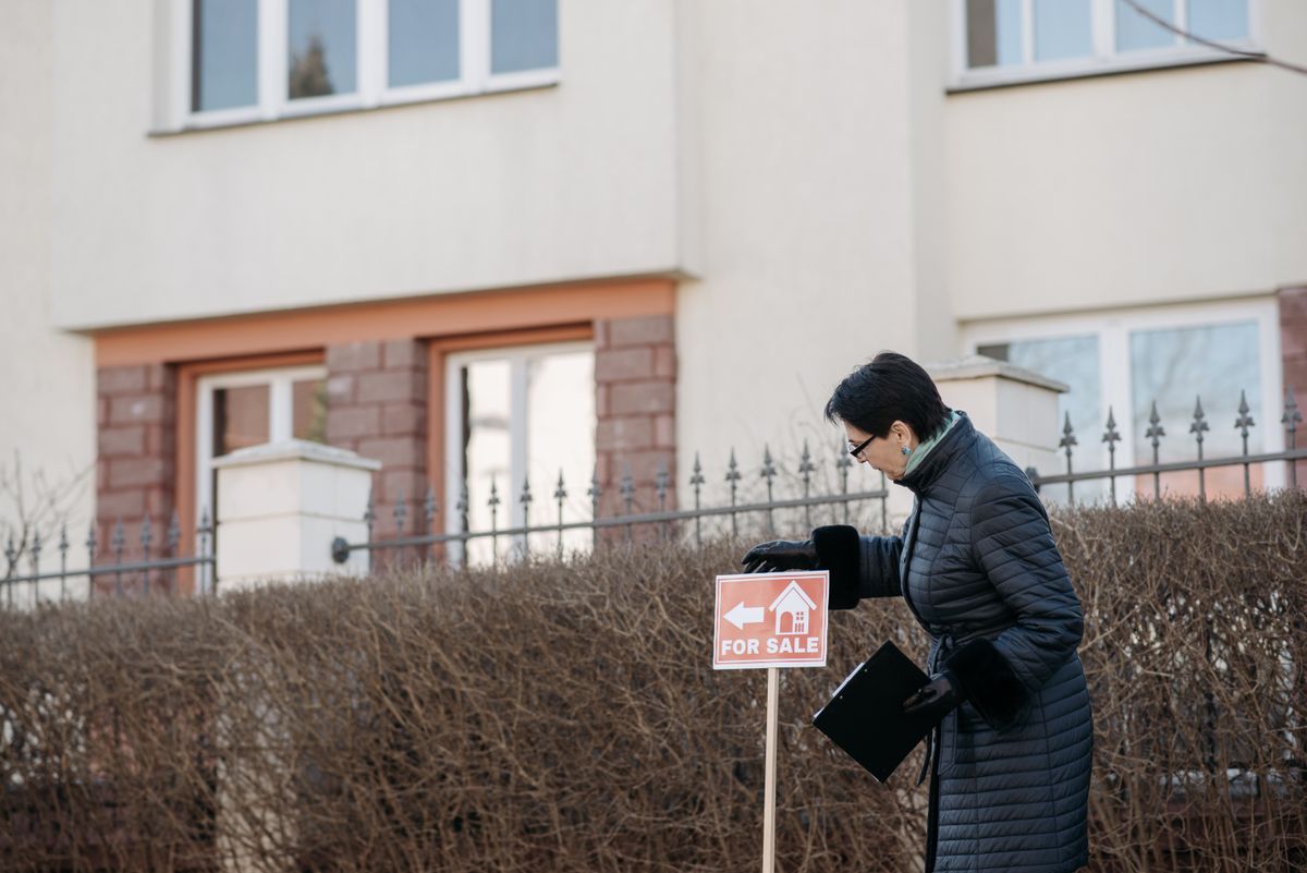 An agent placing a For Sale sign outside a house, the kind of property buyers find after searching on Google