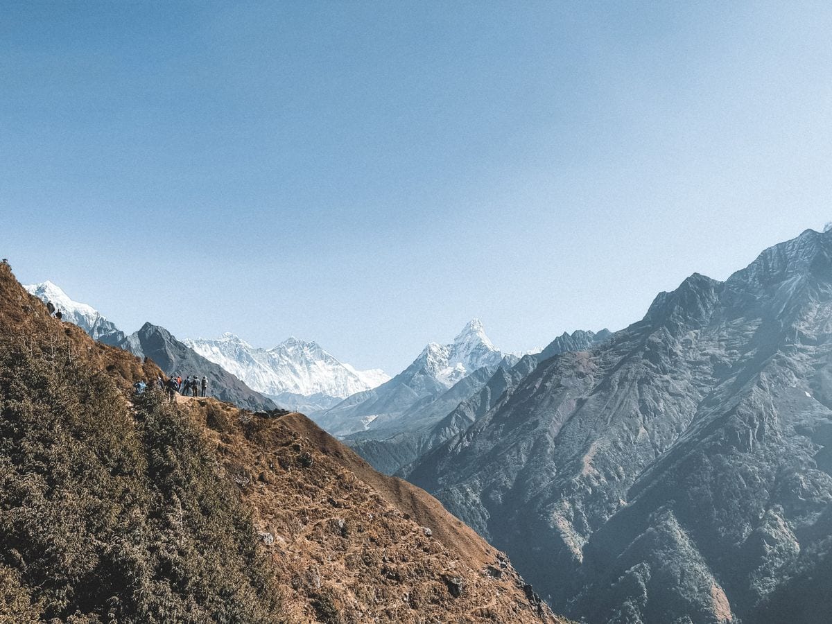 Trekkers on a trail beneath snow-capped Himalayan peaks in Nepal