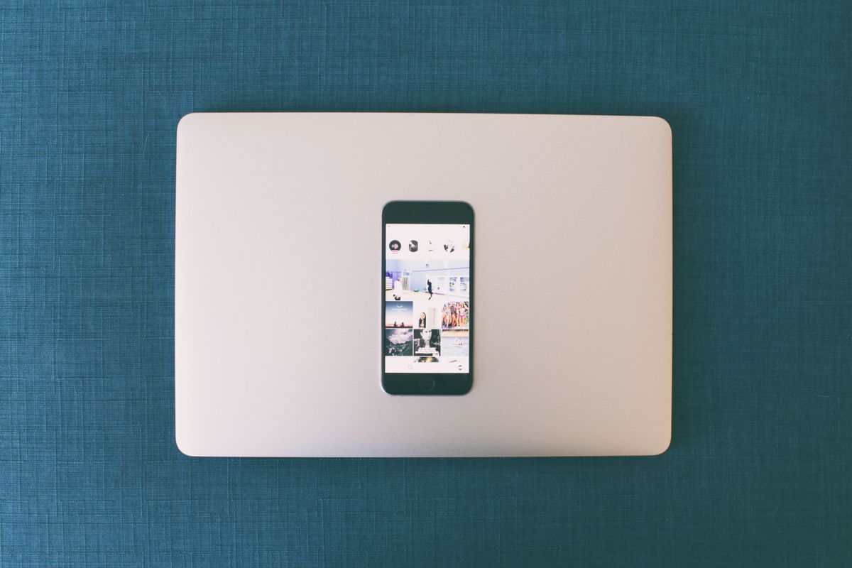 A smartphone resting on a closed laptop, showing a social media feed on its screen